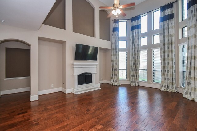 6034 Gracys Landing Ln, Katy, TX 77494 - unfurnished living room with a fireplace with raised hearth, ceiling fan, wood finished floors, a high ceiling, and arched walkways
