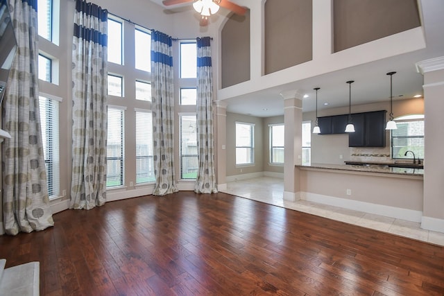 6034 Gracys Landing Ln, Katy, TX 77494 - unfurnished living room featuring ceiling fan, light wood-type flooring, ornate columns, and a towering ceiling