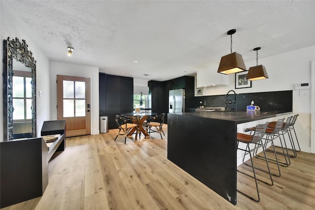 5503 Cheshire Ln, Houston, TX 77092 - kitchen featuring stainless steel fridge, light wood-style flooring, a peninsula, a kitchen bar, and a textured ceiling