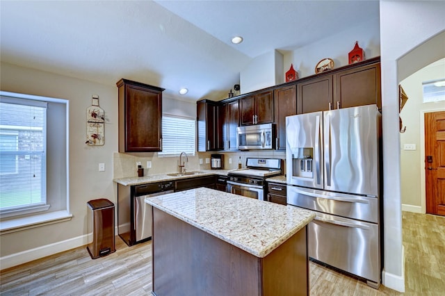 5311 Persimmon Pass, Richmond, TX 77407 - kitchen with appliances with stainless steel finishes, a kitchen island, dark brown cabinetry, light stone countertops, and light wood-style floors