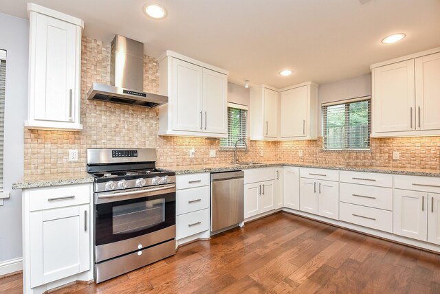 5815 Dryad Dr, Houston, TX 77035 - kitchen with appliances with stainless steel finishes, wall chimney exhaust hood, wood finished floors, white cabinetry, and recessed lighting