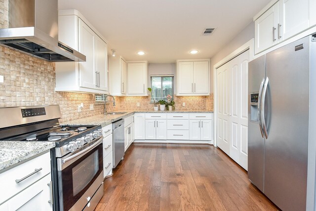 5815 Dryad Dr, Houston, TX 77035 - kitchen featuring stainless steel appliances, wall chimney exhaust hood, white cabinetry, dark wood finished floors, and light stone countertops