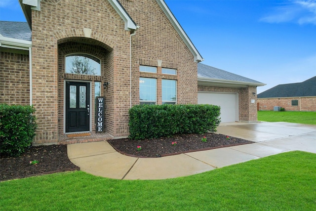 7518 Tejas Lakes Trl, Needville, TX 77461 - view of exterior entry with brick siding, concrete driveway, an attached garage, a yard, and a shingled roof