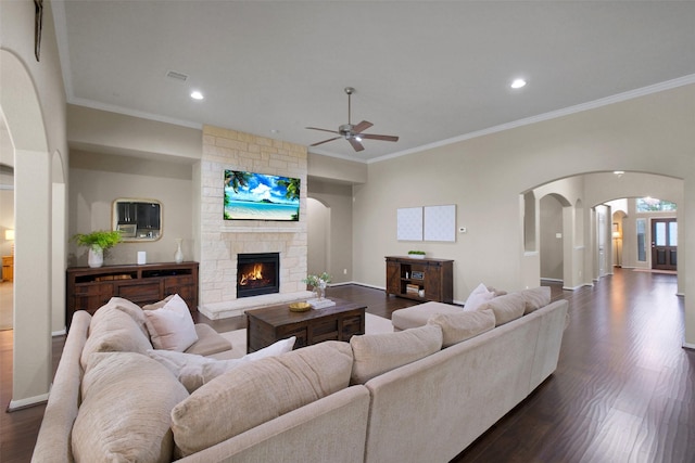 7518 Tejas Lakes Trl, Needville, TX 77461 - living room featuring arched walkways, ceiling fan, dark wood finished floors, a stone fireplace, and ornamental molding