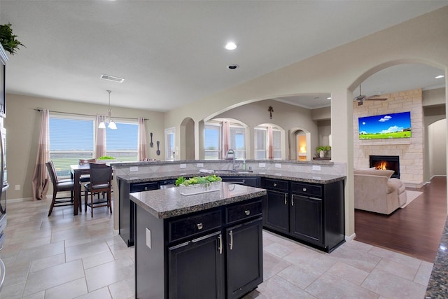 7518 Tejas Lakes Trl, Needville, TX 77461 - kitchen with dark cabinets, a center island, a stone fireplace, light stone counters, and recessed lighting
