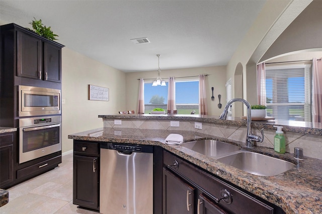 7518 Tejas Lakes Trl, Needville, TX 77461 - kitchen with appliances with stainless steel finishes, dark stone countertops, light tile patterned flooring, dark brown cabinets, and hanging light fixtures