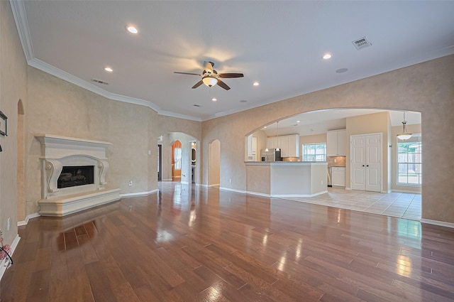 14610 Sandler Ct, Cypress, TX 77429 - unfurnished living room featuring a ceiling fan, light wood-type flooring, arched walkways, crown molding, and a premium fireplace
