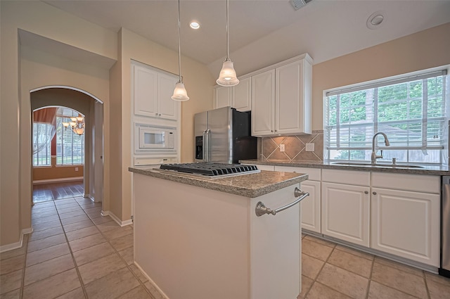 14610 Sandler Ct, Cypress, TX 77429 - kitchen featuring appliances with stainless steel finishes, a center island, backsplash, arched walkways, and white cabinetry