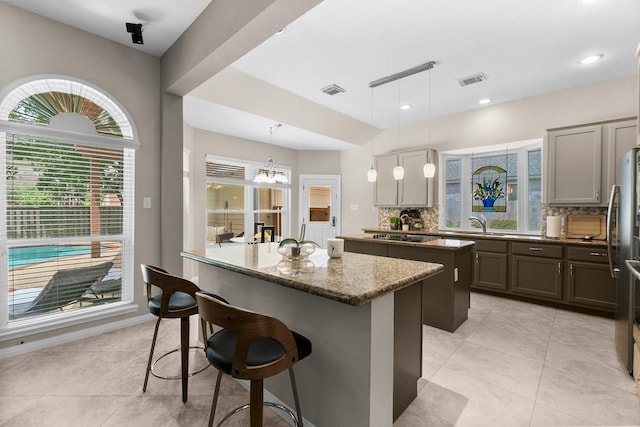 23 Sparklewood Pl, The Woodlands, TX 77381 - kitchen featuring a center island, tasteful backsplash, a kitchen breakfast bar, stone countertops, and light tile patterned flooring