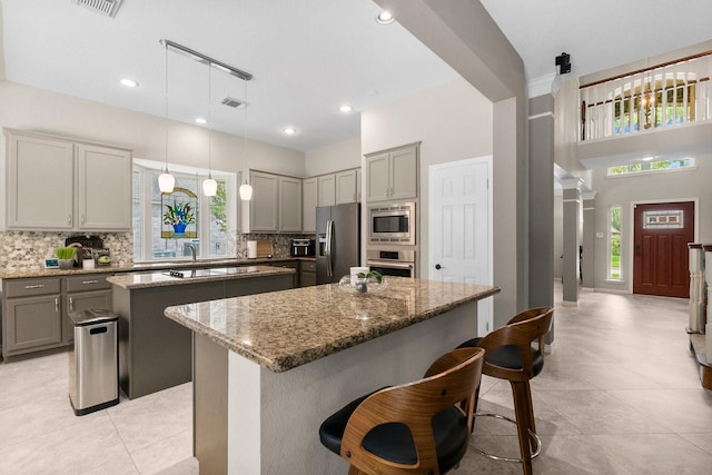 23 Sparklewood Pl, The Woodlands, TX 77381 - kitchen with a kitchen island, appliances with stainless steel finishes, gray cabinetry, tasteful backsplash, and stone countertops