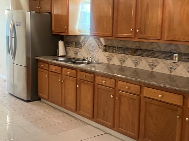 7001 Kassarine Pass, Houston, TX 77033 - kitchen featuring backsplash, brown cabinetry, freestanding refrigerator, dark countertops, and light tile patterned floors