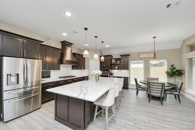 203 Pinedale Ave, Arcola, TX 77583 - kitchen featuring stainless steel appliances, custom exhaust hood, dark brown cabinets, decorative backsplash, and light stone countertops