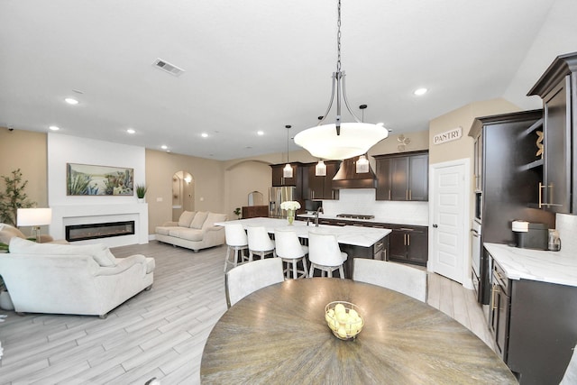 203 Pinedale Ave, Arcola, TX 77583 - dining room with arched walkways, recessed lighting, a glass covered fireplace, and light wood finished floors