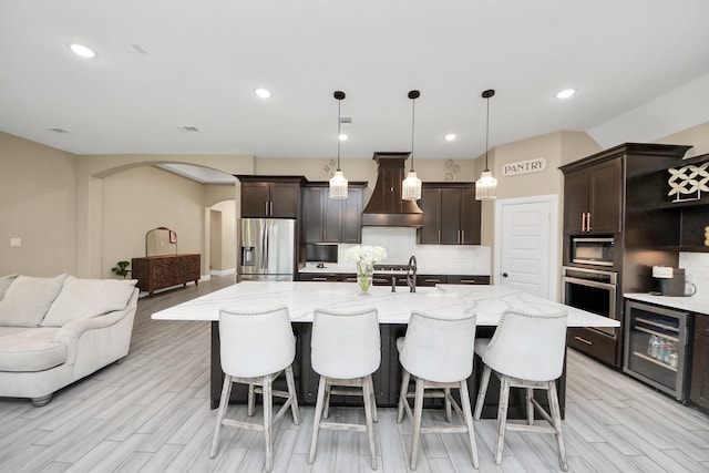 203 Pinedale Ave, Arcola, TX 77583 - kitchen featuring wine cooler, premium range hood, stainless steel appliances, arched walkways, and tasteful backsplash