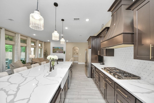 203 Pinedale Ave, Arcola, TX 77583 - kitchen with appliances with stainless steel finishes, premium range hood, open floor plan, arched walkways, and dark brown cabinetry