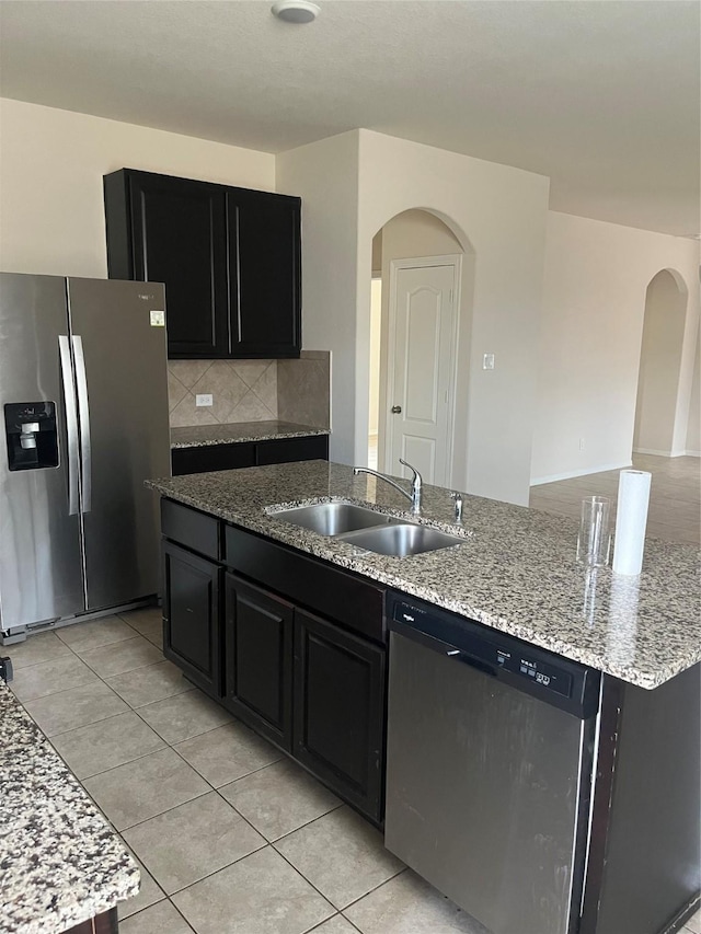2135 Republic Way, Missouri City, TX 77489 - kitchen featuring stainless steel appliances, dark cabinets, arched walkways, backsplash, and light stone counters