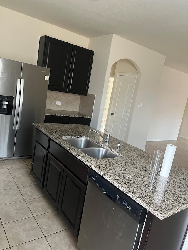 2135 Republic Way, Missouri City, TX 77489 - kitchen with appliances with stainless steel finishes, dark cabinetry, arched walkways, light stone counters, and light tile patterned floors