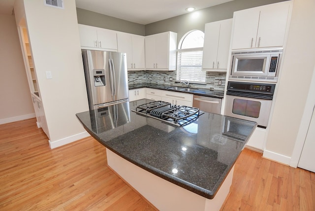 9703 Riddlewood Ln, Houston, TX 77025 - kitchen featuring appliances with stainless steel finishes, light wood finished floors, decorative backsplash, a kitchen island, and white cabinets