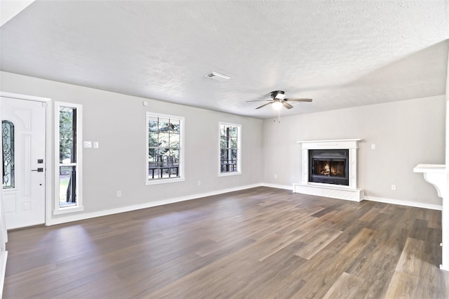 387 Hackberry Dr, Onalaska, TX 77360 - unfurnished living room with dark wood-style flooring, a textured ceiling, a ceiling fan, and a glass covered fireplace