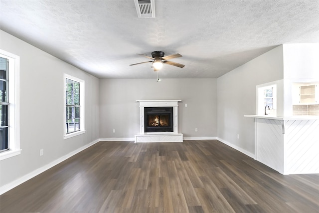 387 Hackberry Dr, Onalaska, TX 77360 - unfurnished living room featuring dark wood-style floors, a ceiling fan, a warm lit fireplace, and a textured ceiling