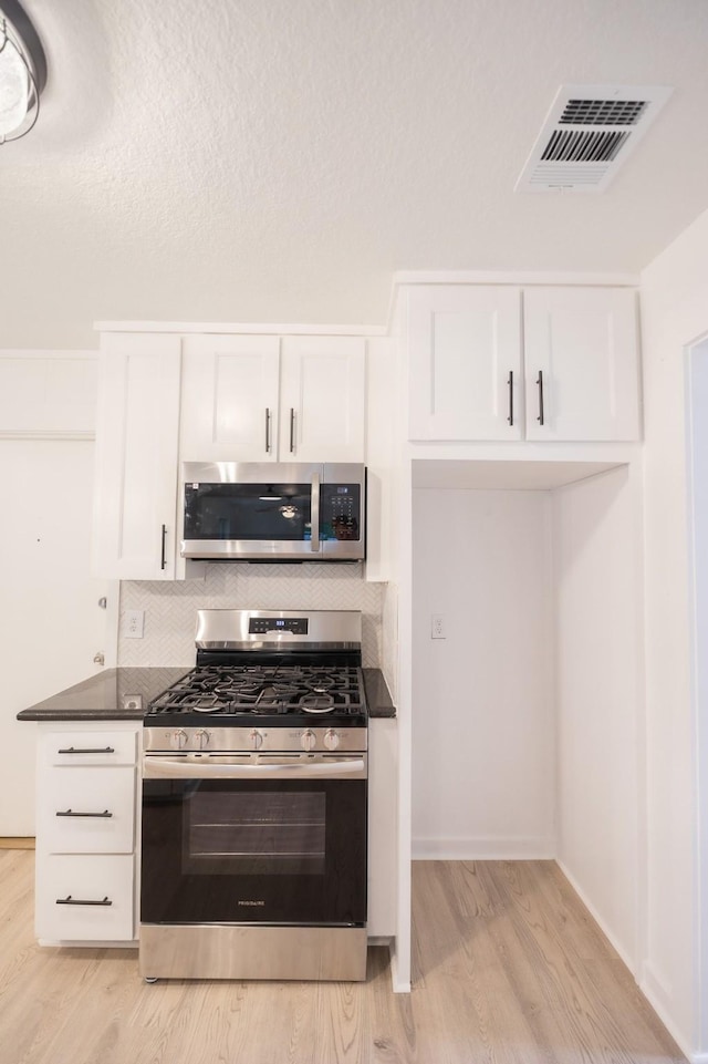1025 Hathaway Ln, Marque, TX 77568 - kitchen featuring appliances with stainless steel finishes, dark countertops, light wood-style flooring, white cabinetry, and tasteful backsplash
