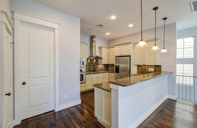 517 Fowler St, Houston, TX 77007 - kitchen with appliances with stainless steel finishes, wall chimney range hood, dark wood-type flooring, dark stone counters, and a peninsula