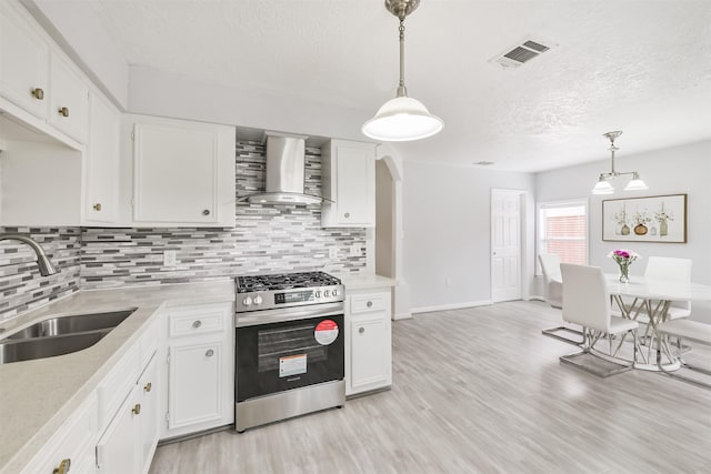 10329 Fairfax St, Houston, TX 77029 - kitchen featuring stainless steel gas range oven, wall chimney range hood, light wood-type flooring, light countertops, and a textured ceiling