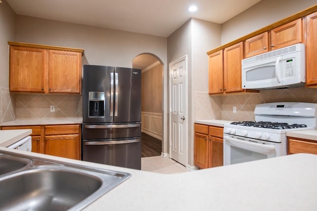 30615 S Sulphur Creek Dr, Magnolia, TX 77355 - kitchen with white appliances, arched walkways, light countertops, brown cabinetry, and backsplash