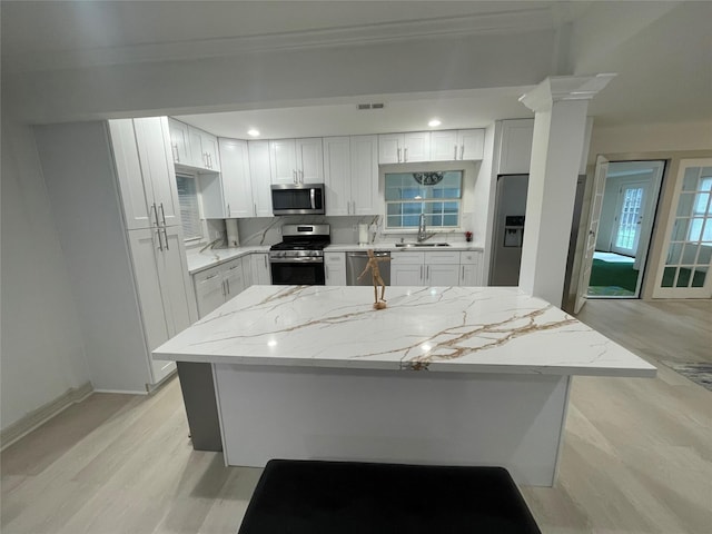12834 Tosca Ln, Houston, TX 77024 - kitchen featuring stainless steel appliances, light stone counters, light wood-style flooring, white cabinetry, and crown molding