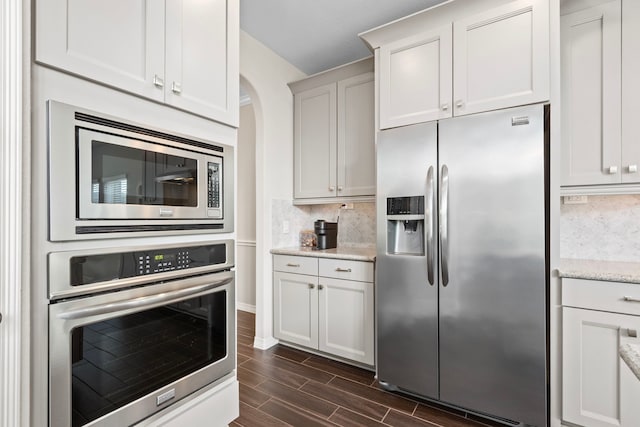 6303 Grand Drift Ct, Katy, TX 77494 - kitchen featuring appliances with stainless steel finishes, wood tiled floors, tasteful backsplash, light stone counters, and arched walkways