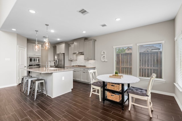 6303 Grand Drift Ct, Katy, TX 77494 - kitchen with stainless steel appliances, under cabinet range hood, gray cabinets, a breakfast bar, and tasteful backsplash