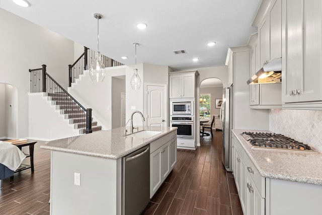 6303 Grand Drift Ct, Katy, TX 77494 - kitchen with appliances with stainless steel finishes, arched walkways, under cabinet range hood, dark wood finished floors, and backsplash