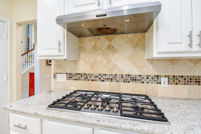 1006 Pointe Loma Dr, Sugar Land, TX 77479 - kitchen with under cabinet range hood, stainless steel gas cooktop, white cabinetry, and decorative backsplash