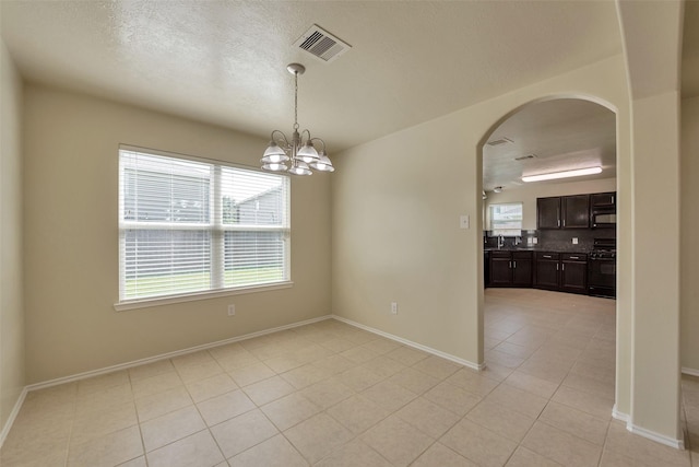 12807 Maybank Shores Ct, Houston, TX 77045 - empty room featuring light tile patterned floors, arched walkways, a chandelier, and a textured ceiling