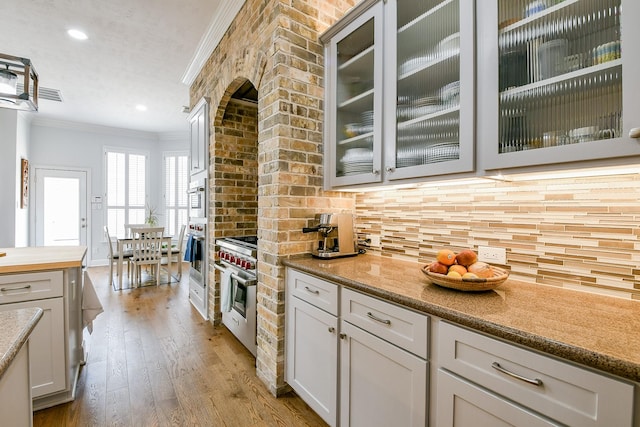 2442 Chimney Rock Rd, Houston, TX 77056 - kitchen with crown molding, glass insert cabinets, decorative backsplash, wood-type flooring, and premium stove