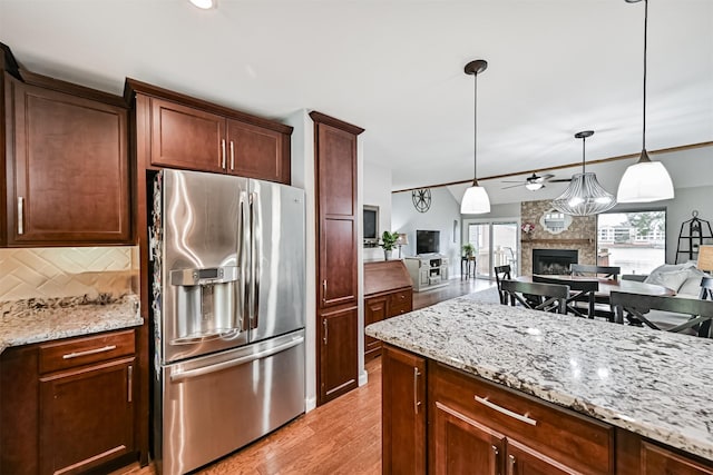 2114 Crows Nest Dr, League City, TX 77573 - kitchen with stainless steel fridge with ice dispenser, backsplash, a fireplace, a ceiling fan, and light stone countertops