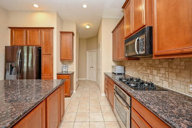 21211 Dover Park Ln, Katy, TX 77450 - kitchen featuring stainless steel appliances, tasteful backsplash, light tile patterned floors, brown cabinets, and dark stone countertops