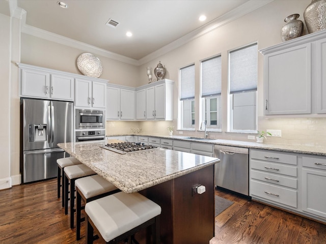 249 E 27th St, Houston, TX 77008 - kitchen featuring appliances with stainless steel finishes, ornamental molding, a center island, light stone counters, and a kitchen bar