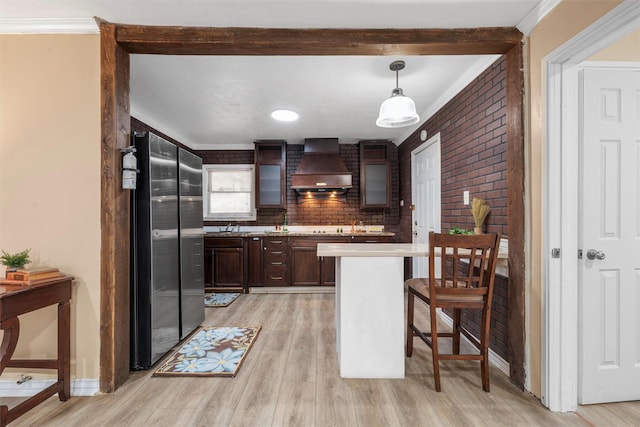 4505 Memorial Dr, Waco, TX 76711 - kitchen featuring wall chimney exhaust hood, light countertops, a breakfast bar, dark brown cabinetry, and ornamental molding