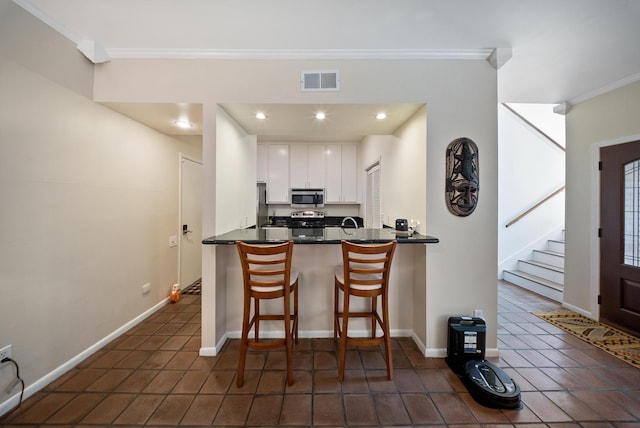 4904 Feagan St Unit 1, Houston, TX 77007 - kitchen featuring stainless steel appliances, dark countertops, white cabinetry, ornamental molding, and a breakfast bar area