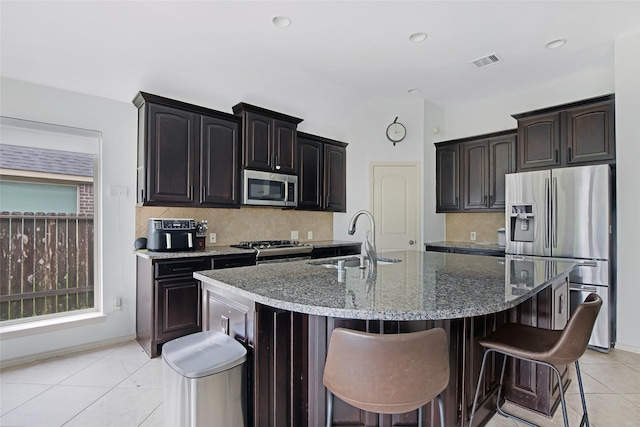 13015 Barkley Bend Ln, Houston, TX 77044 - kitchen with stainless steel appliances, a kitchen bar, decorative backsplash, dark stone countertops, and light tile patterned floors