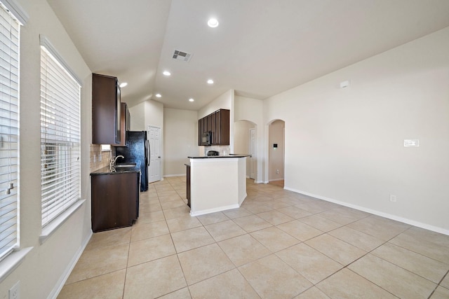 19842 Haven Cliff Ln, Cypress, TX 77433 - kitchen featuring dark countertops, arched walkways, dark brown cabinets, light tile patterned floors, and decorative backsplash