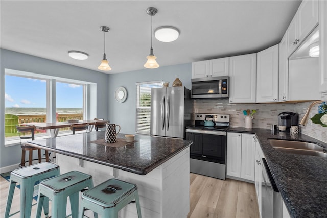 21446 Gulf Dr, Galveston, TX 77554 - kitchen with appliances with stainless steel finishes, light wood-style flooring, white cabinetry, backsplash, and a kitchen bar