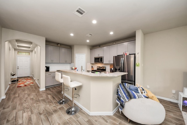 7947 Cinderella St, Houston, TX 77028 - kitchen featuring stainless steel appliances, arched walkways, light wood-style floors, backsplash, and a kitchen bar