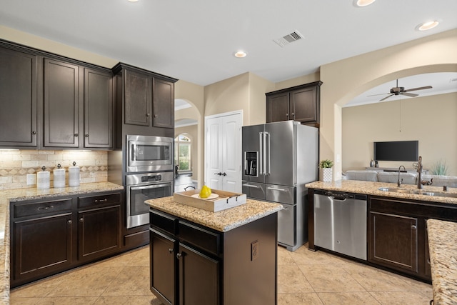 10527 Caddo Lake Dr, Needville, TX 77461 - kitchen featuring appliances with stainless steel finishes, arched walkways, a ceiling fan, light stone counters, and recessed lighting