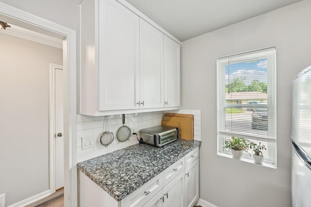 10676 Hazelhurst Dr, Houston, TX 77043 - kitchen with freestanding refrigerator, decorative backsplash, white cabinets, dark stone countertops, and light wood-style flooring