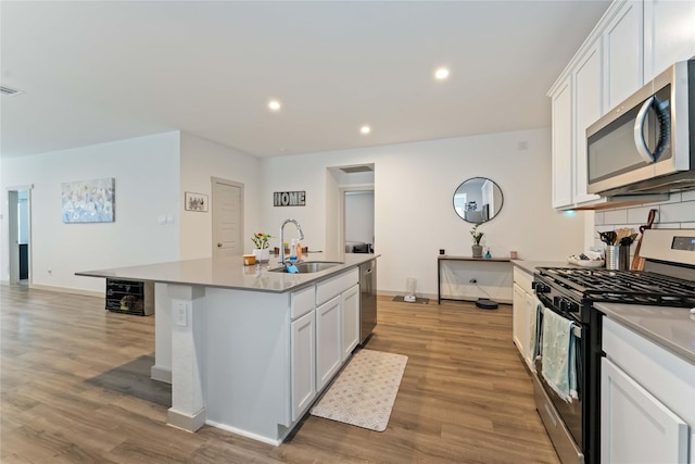 7902 Sleek Flock Ln, Rosharon, TX 77583 - kitchen with stainless steel appliances, white cabinets, light wood-style flooring, a center island with sink, and recessed lighting