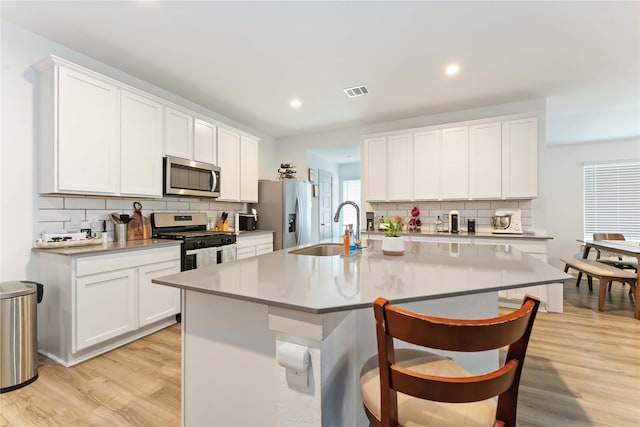 7902 Sleek Flock Ln, Rosharon, TX 77583 - kitchen featuring stainless steel appliances, decorative backsplash, light wood-style flooring, a kitchen island with sink, and a kitchen breakfast bar