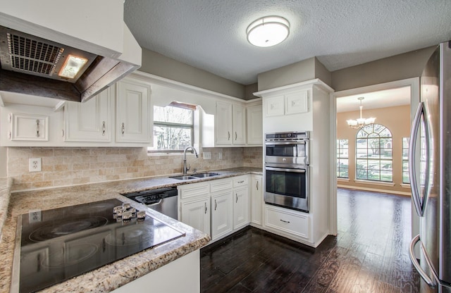 1511 Calveryman Ln, Katy, TX 77449 - kitchen featuring appliances with stainless steel finishes, exhaust hood, dark wood-style flooring, white cabinetry, and a chandelier