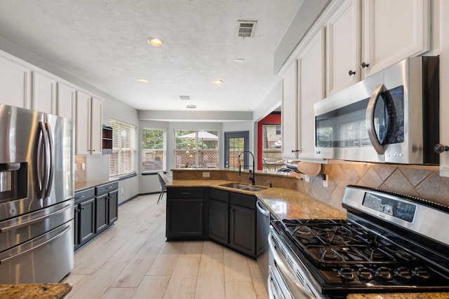 96 N Acacia Park Cir, The Woodlands, TX 77382 - kitchen featuring stainless steel appliances, white cabinetry, a peninsula, tasteful backsplash, and light stone counters